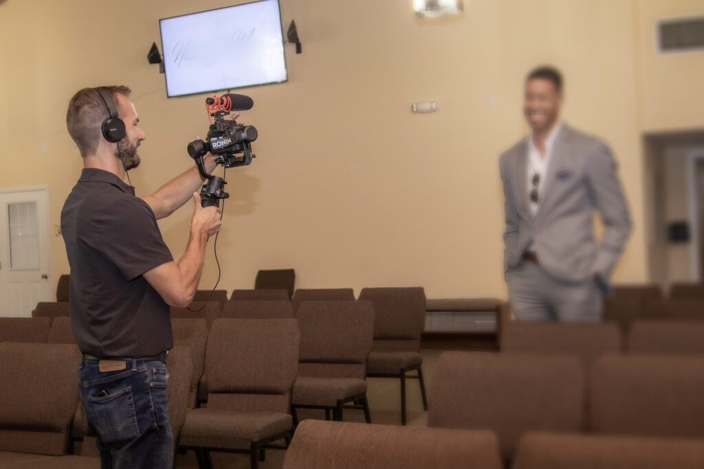 Videographer Davey Rockwell captures a groomsman walking down a church aisle during the processional at a wedding, using a Canon DSLR 90D, a Ronin Gimble Mount and a Rode shotgun mic